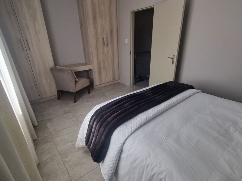 A well-maintained bedroom featuring neutral tiled flooring, built-in wooden cupboards, and an integrated vanity unit.