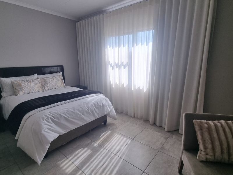 A well-maintained bedroom featuring neutral tiled flooring, a built-in wardrobe, and floor-to-ceiling curtains providing natural light control.