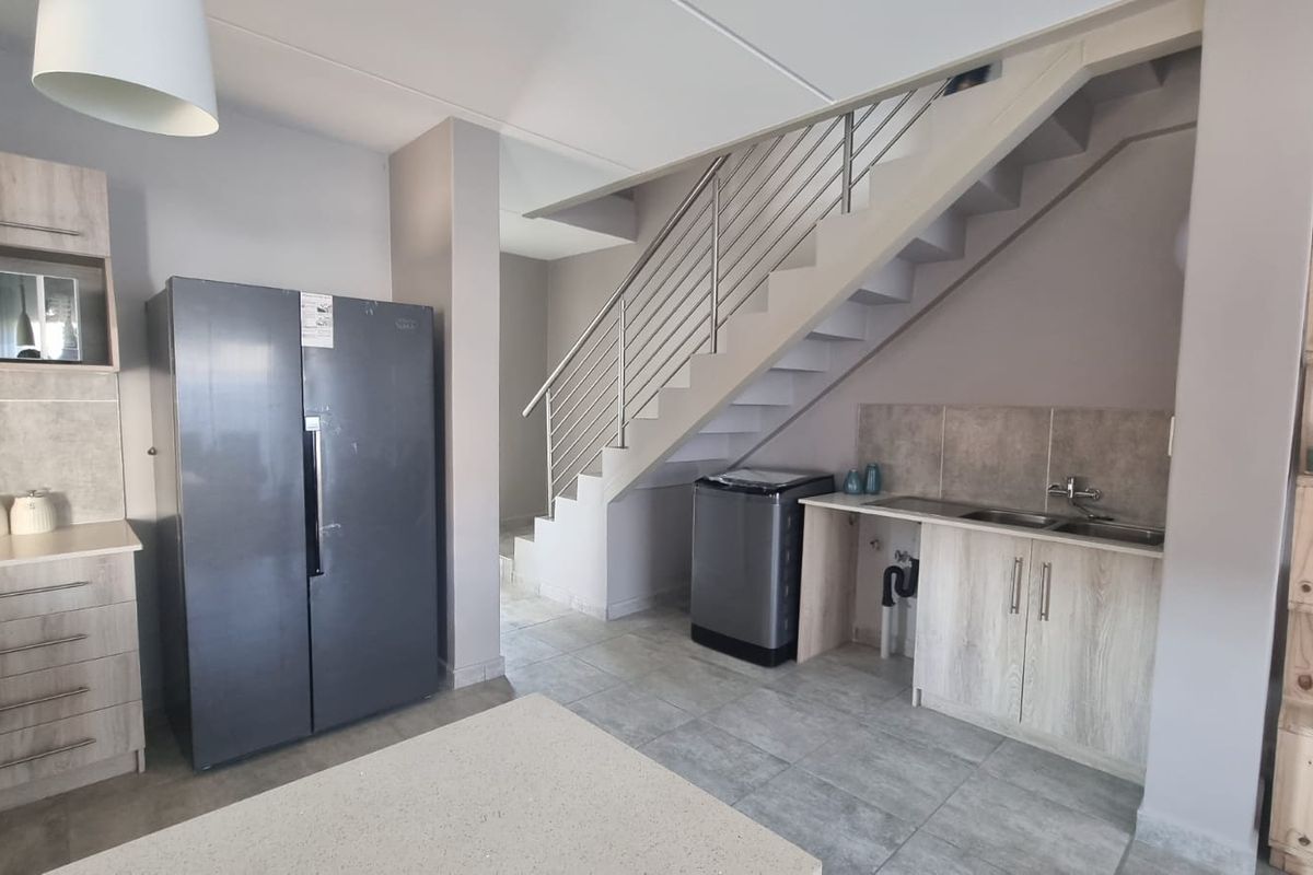 A functional kitchen area featuring built-in cabinetry, a double sink, and tiled finishes, conveniently located beneath an open-plan staircase.