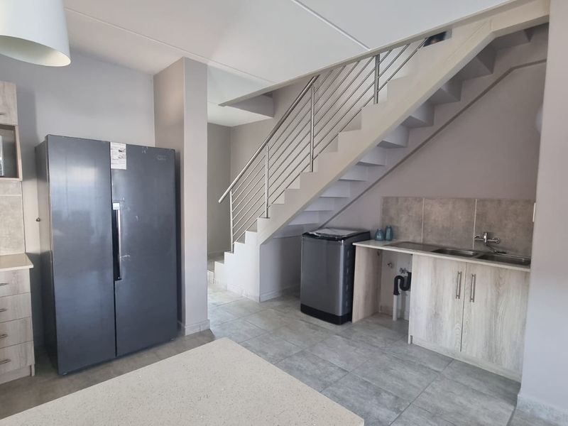 A functional kitchen area featuring built-in cabinetry, a double sink, and tiled finishes, conveniently located beneath an open-plan staircase.