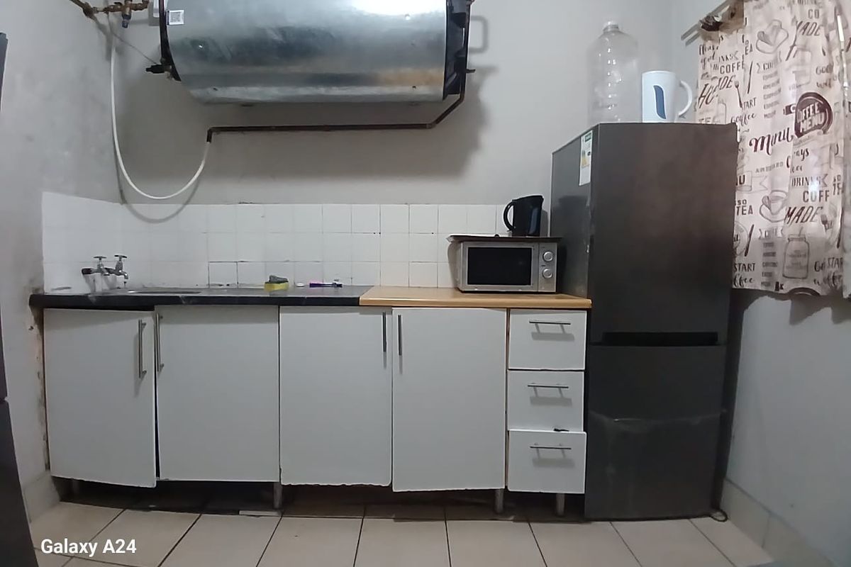 A compact kitchen area featuring basic cabinetry, a sink, tiled backsplash, and an exposed wall-mounted electric water heater.