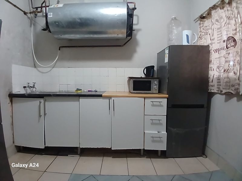 A compact kitchen area featuring basic cabinetry, a sink, tiled backsplash, and an exposed wall-mounted electric water heater.