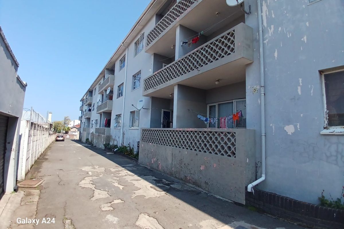 Rear view of an apartment building featuring concrete balconies with decorative breeze block balustrades and a weathered asphalt driveway.