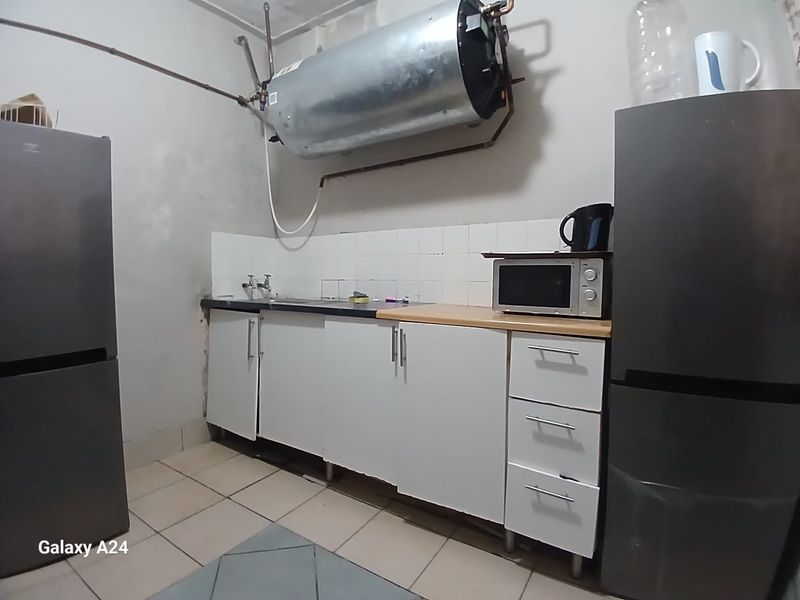 A functional kitchen area featuring basic cabinetry, a sink, and an exposed electric water heater, requiring cosmetic updates and maintenance.
