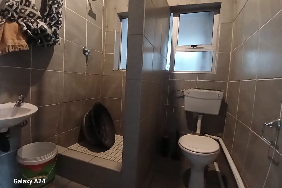 A compact bathroom featuring a shower area, wall-mounted basin, and toilet, requiring significant cosmetic updates and finishing of exposed plumbing and wall surfaces.