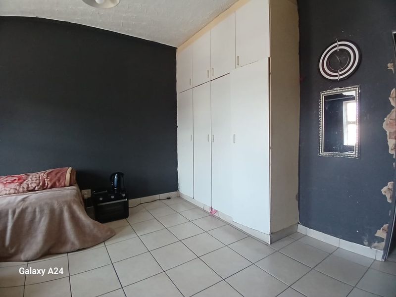 Bedroom featuring built-in cupboards and tiled flooring, currently showing signs of wall surface damage and peeling paint.