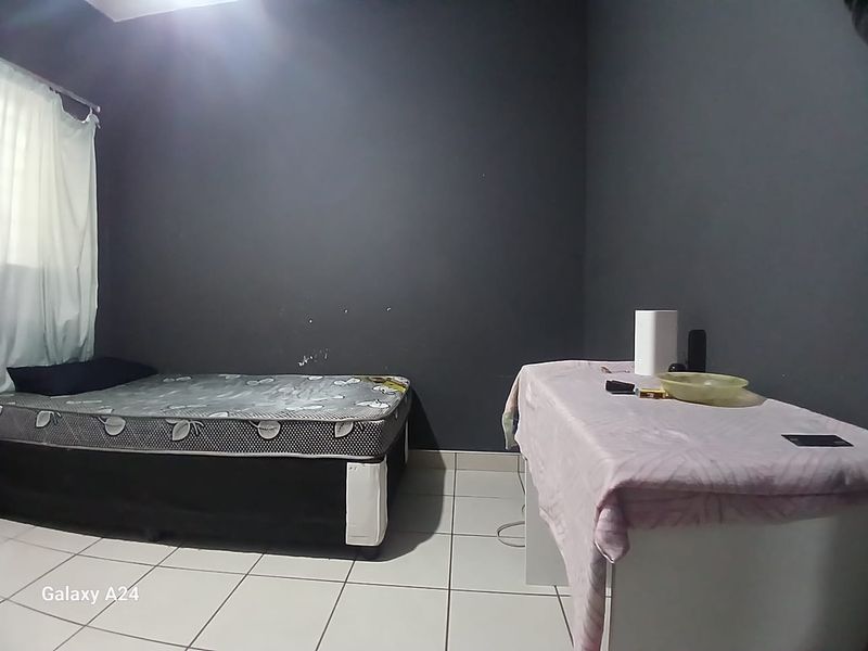 A bedroom featuring dark painted walls and tiled flooring, currently furnished with a bed and a table.