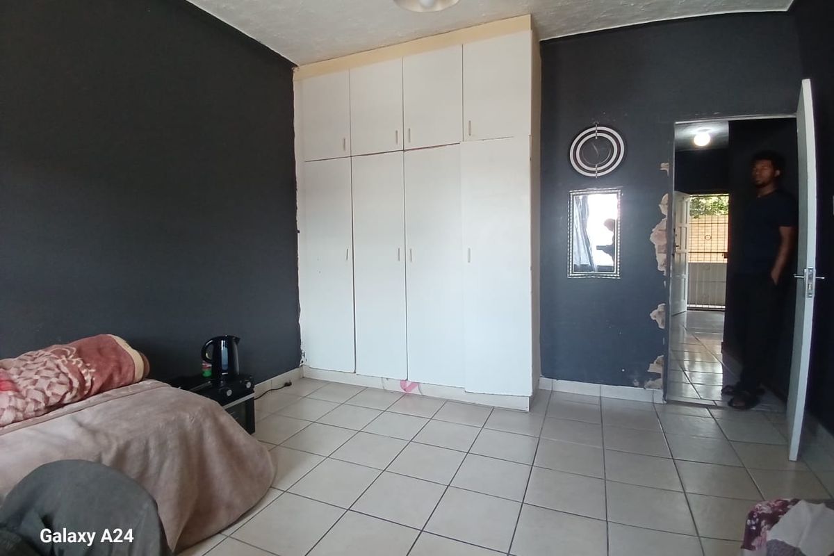 Bedroom featuring built-in cupboards and tiled flooring, requiring some wall repairs and cosmetic updates to improve the overall finish.