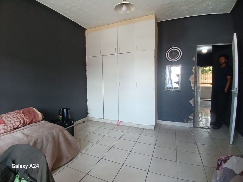 Bedroom featuring built-in cupboards and tiled flooring, requiring some wall repairs and cosmetic updates to improve the overall finish.