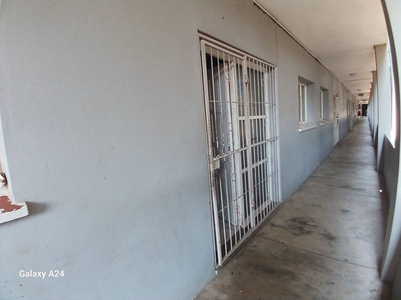 An exterior-facing apartment hallway featuring concrete flooring and security gates installed on the unit entrance.