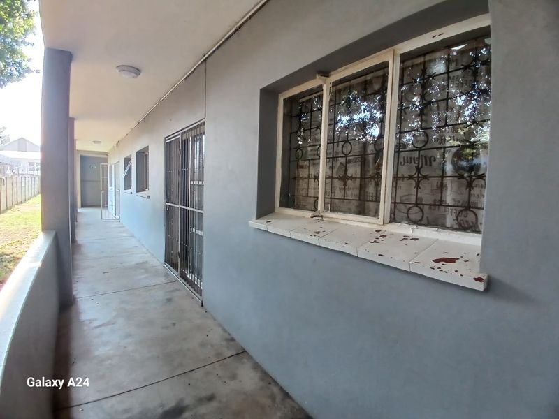 An exterior walkway or balcony area featuring concrete flooring, security gates, and security bars on the windows.