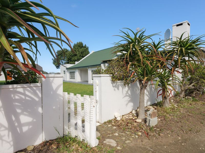 Front view of a house featuring a white boundary wall, gated entrance, green pitched roof, and a well-maintained lawn.