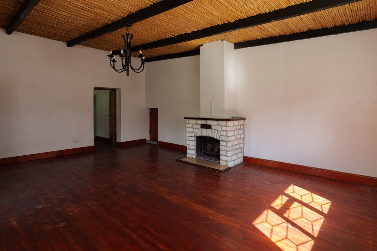 Spacious living room featuring a rustic reed ceiling with exposed beams, a brick fireplace, and original hardwood flooring.