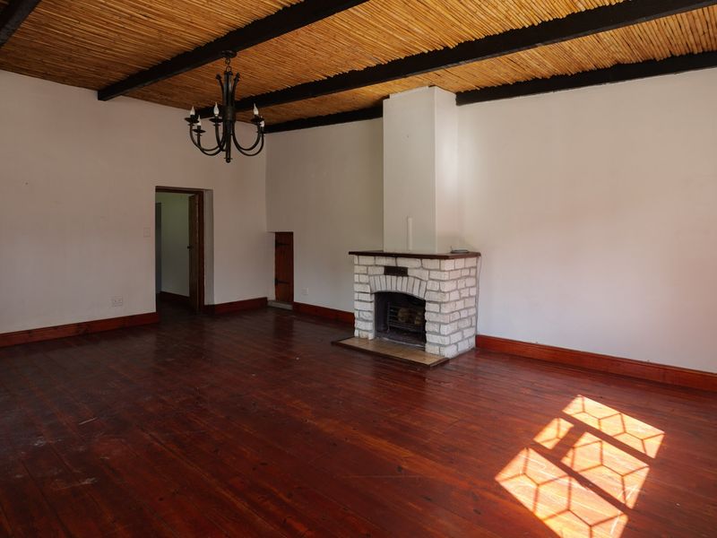 Spacious living room featuring a rustic reed ceiling with exposed beams, a brick fireplace, and original hardwood flooring.