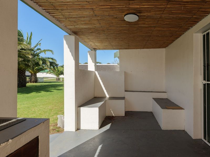 Covered outdoor patio featuring a built-in braai, integrated concrete seating, and a bamboo ceiling, overlooking a landscaped garden area.