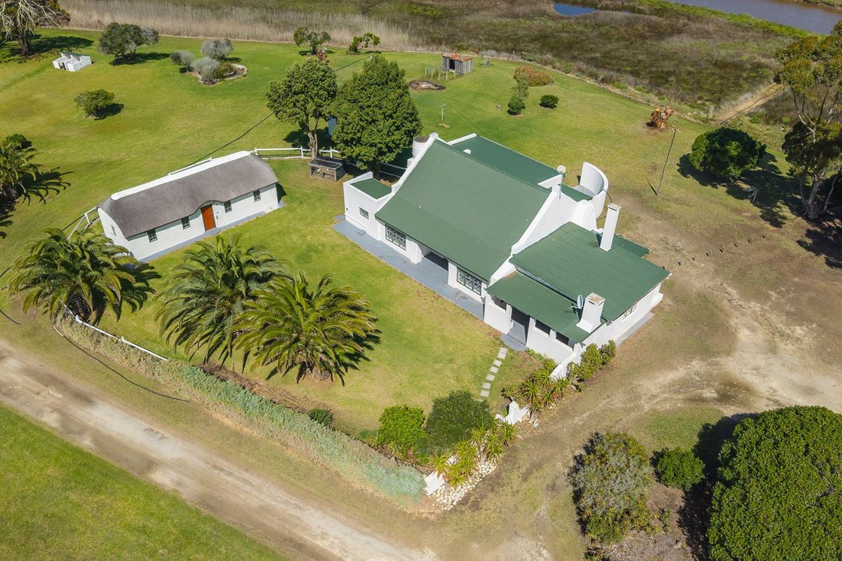 Aerial view of a rural property featuring a main house with a green metal roof, a separate thatched outbuilding, and expansive surrounding grounds.