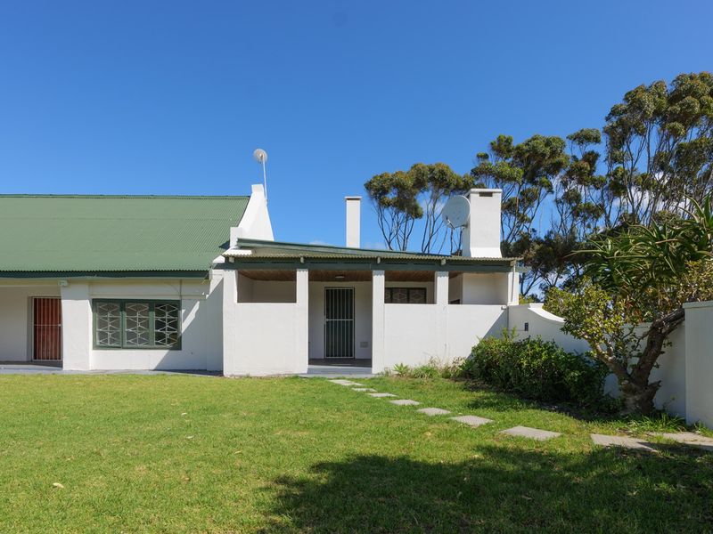 Rear view of a house featuring a green corrugated metal roof, a covered patio area, and a well-maintained lawn with a stone pathway.