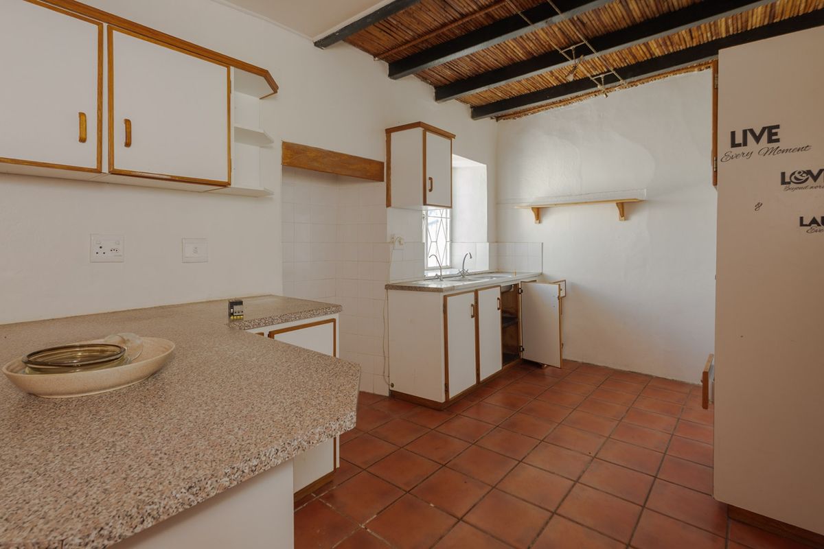 A dated kitchen featuring built-in cabinetry, laminate countertops, a double basin sink, and exposed timber beams, offering significant potential for modernization.