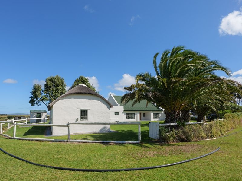 A charming rural property featuring a traditional thatched-roof cottage and a main house with a green metal roof, set within a spacious garden.