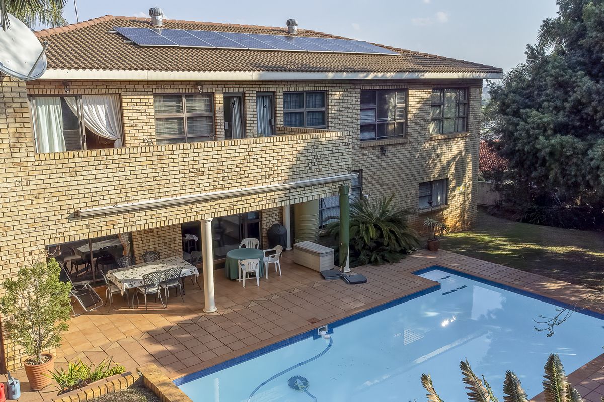 Rear view of a double-story brick house featuring a swimming pool, tiled patio area, upper-level balcony, and roof-mounted solar panels.
