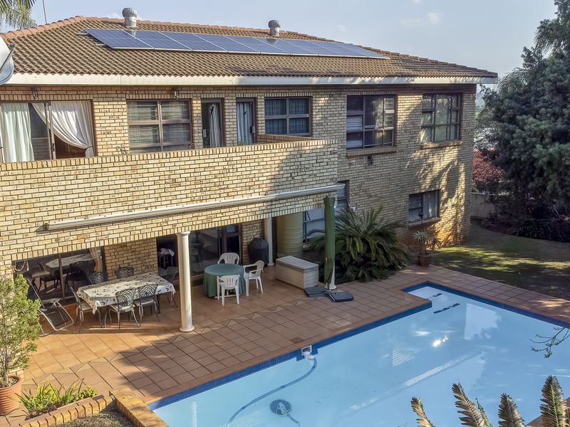 Rear view of a double-story brick house featuring a swimming pool, tiled patio area, upper-level balcony, and roof-mounted solar panels.