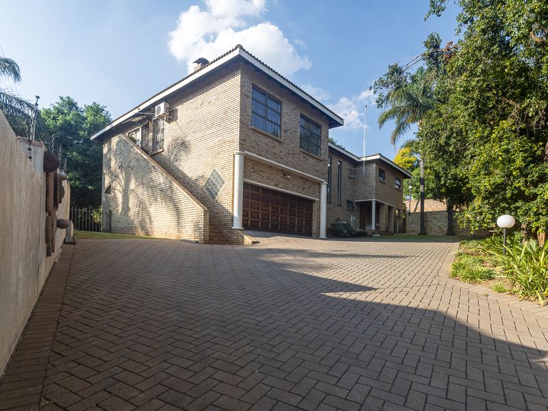 Front view of a double-story brick house featuring a paved driveway, double garage, and secure perimeter fencing.