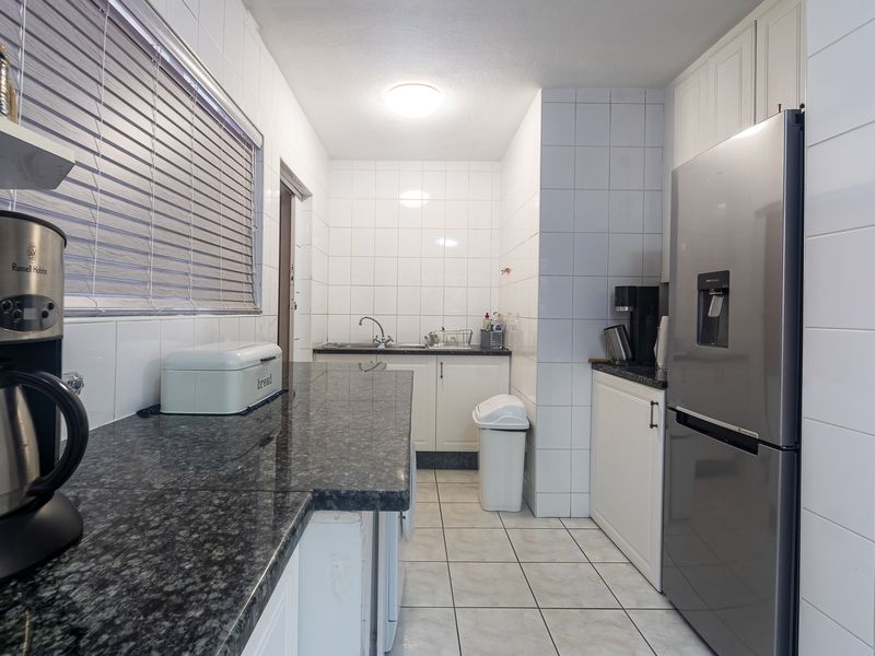 A functional kitchen featuring granite countertops, white tiled walls, and tiled flooring, offering a clean and practical workspace.