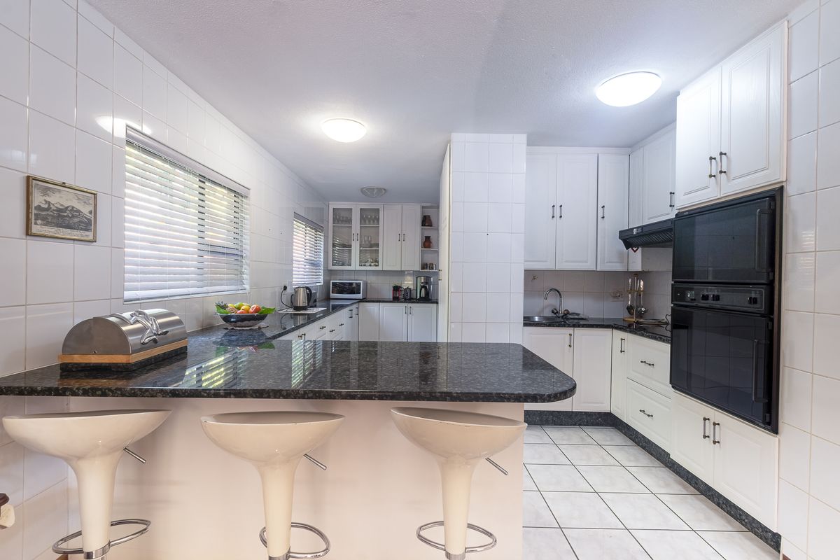 A functional kitchen featuring white cabinetry, granite countertops, a breakfast bar, and a built-in double oven with tiled finishes throughout.