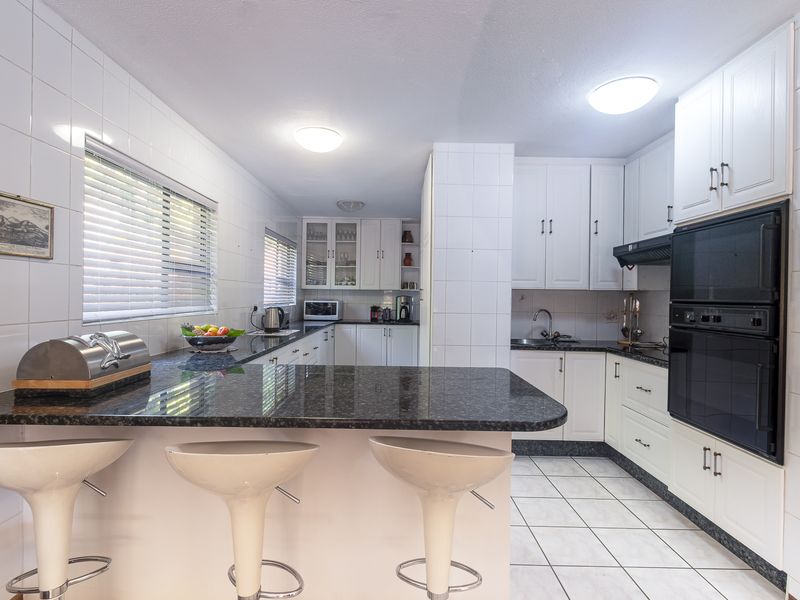 A functional kitchen featuring white cabinetry, granite countertops, a breakfast bar, and a built-in double oven with tiled finishes throughout.