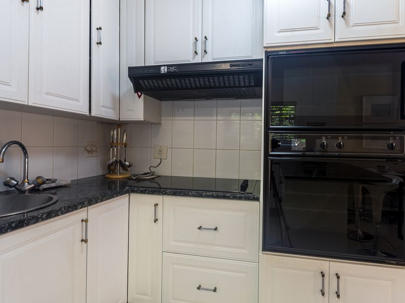 A functional kitchen featuring white cabinetry, granite countertops, a built-in oven, and a tiled backsplash.