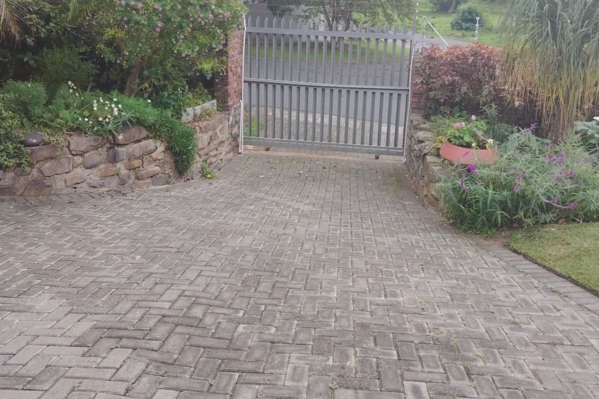 A paved driveway leading to a metal security gate, framed by stone retaining walls and established garden landscaping.