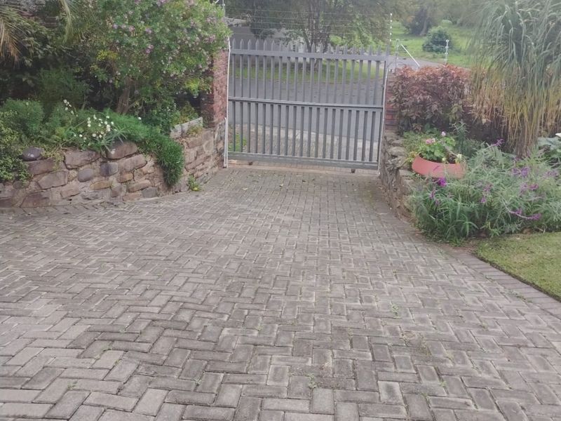 A paved driveway leading to a metal security gate, framed by stone retaining walls and established garden landscaping.