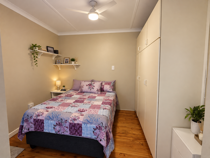 A well-maintained bedroom featuring polished timber flooring, a built-in wardrobe, and a ceiling fan, offering a clean and functional living space.