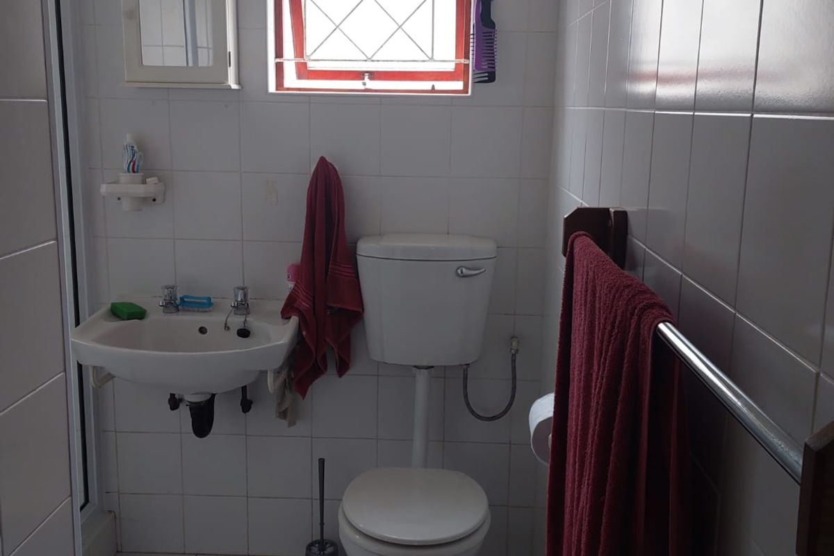 A functional bathroom featuring a wall-mounted basin, standard toilet, and fully tiled walls and floors with a security-grille window.