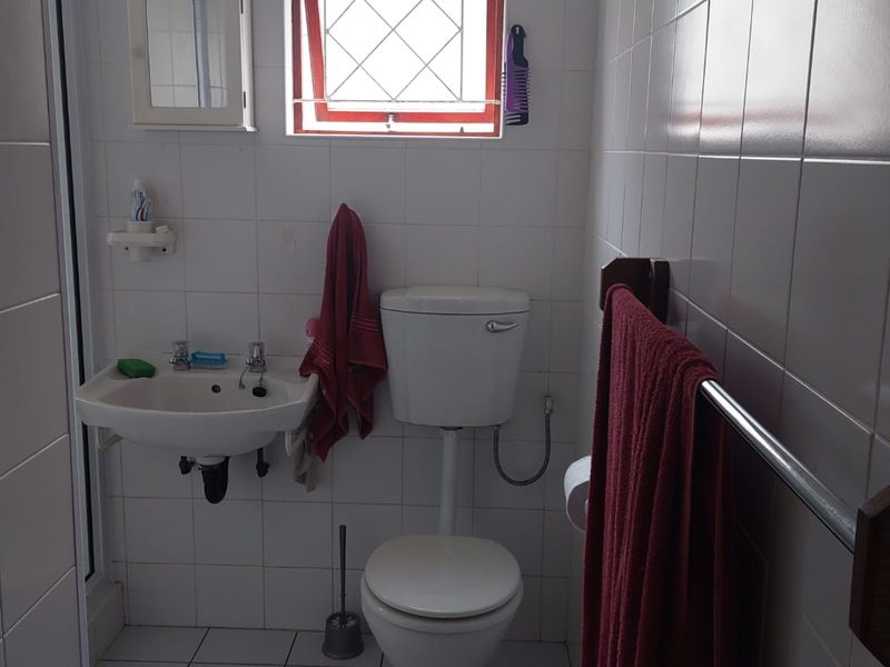 A functional bathroom featuring a wall-mounted basin, standard toilet, and fully tiled walls and floors with a security-grille window.