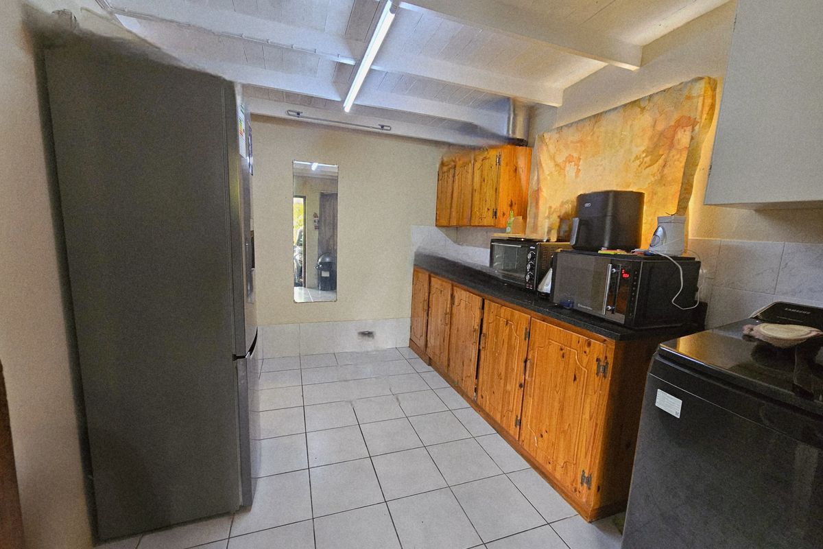 A functional kitchen featuring wooden cabinetry, tiled flooring, and an exposed beam ceiling, offering potential for a modern renovation.