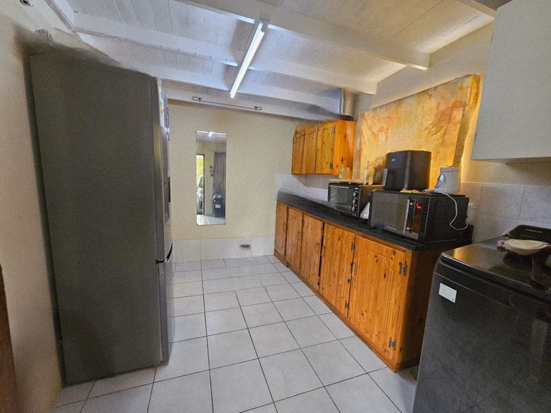 A functional kitchen featuring wooden cabinetry, tiled flooring, and an exposed beam ceiling, offering potential for a modern renovation.