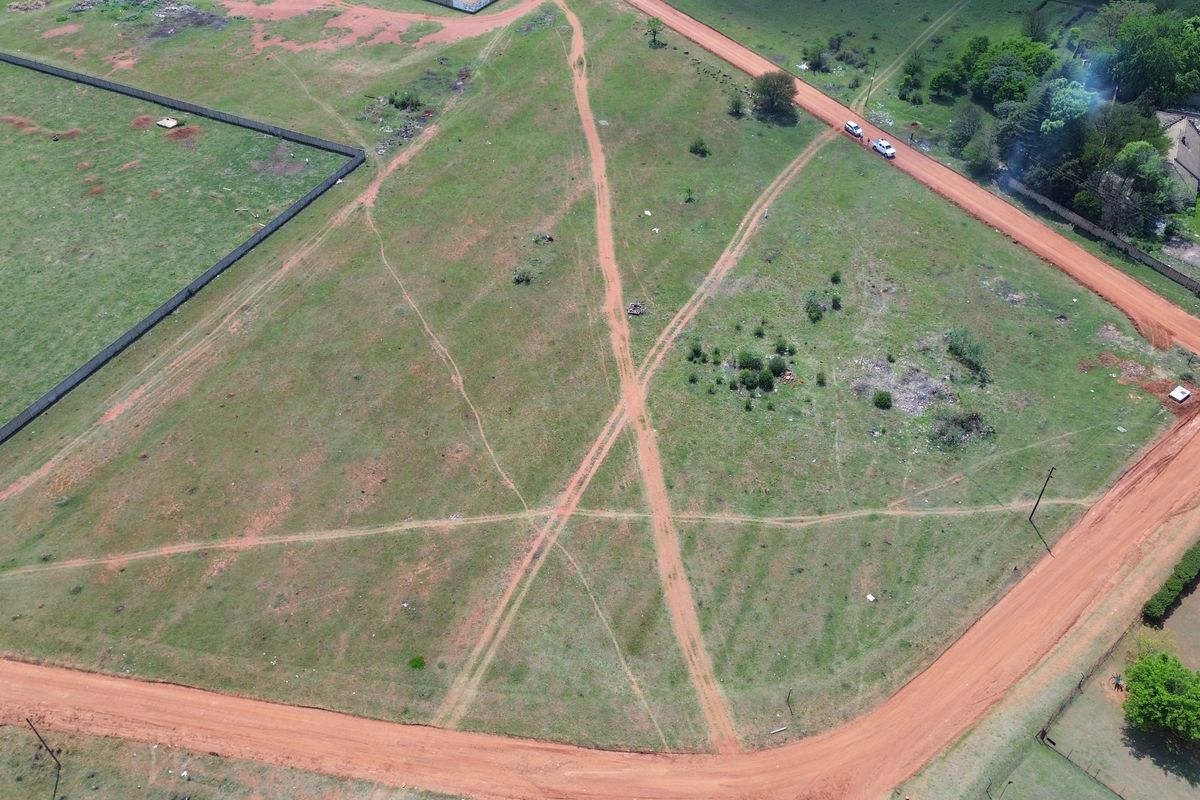 Aerial view of a vacant residential plot featuring dirt road access and perimeter fencing, suitable for future development.