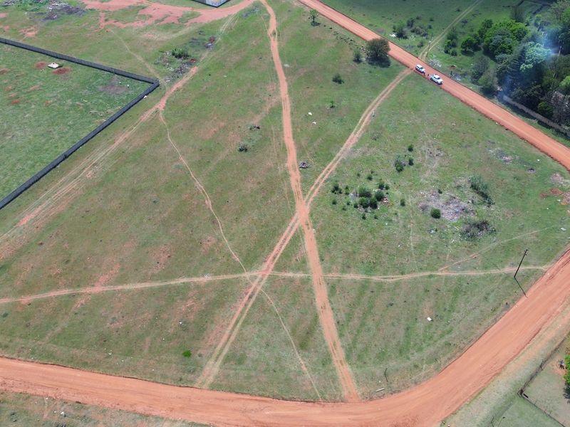 Aerial view of a vacant residential plot featuring dirt road access and perimeter fencing, suitable for future development.