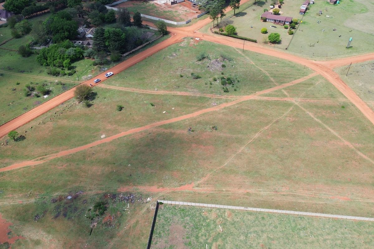 An aerial view of a vacant residential plot featuring surrounding dirt roads and perimeter fencing in a rural setting.