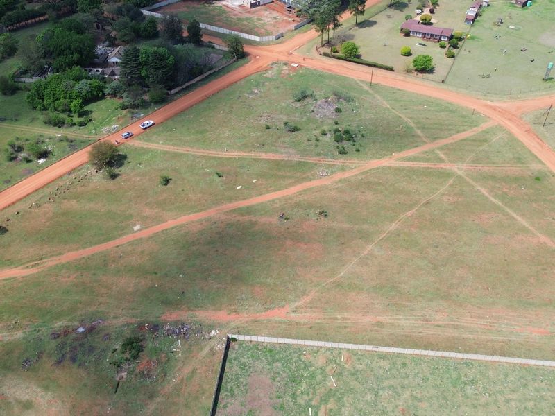 An aerial view of a vacant residential plot featuring surrounding dirt roads and perimeter fencing in a rural setting.