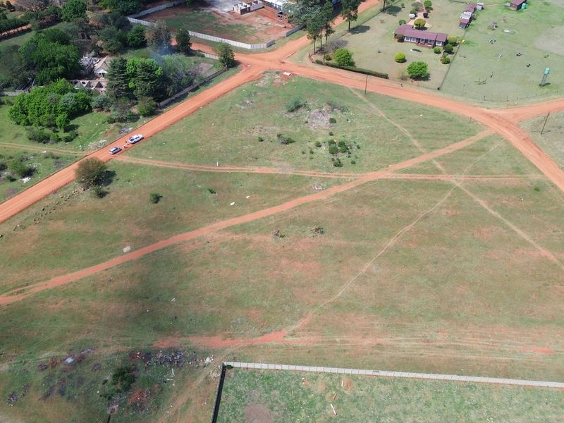 An aerial view of a vacant residential plot featuring natural terrain, dirt access roads, and surrounding perimeter fencing.