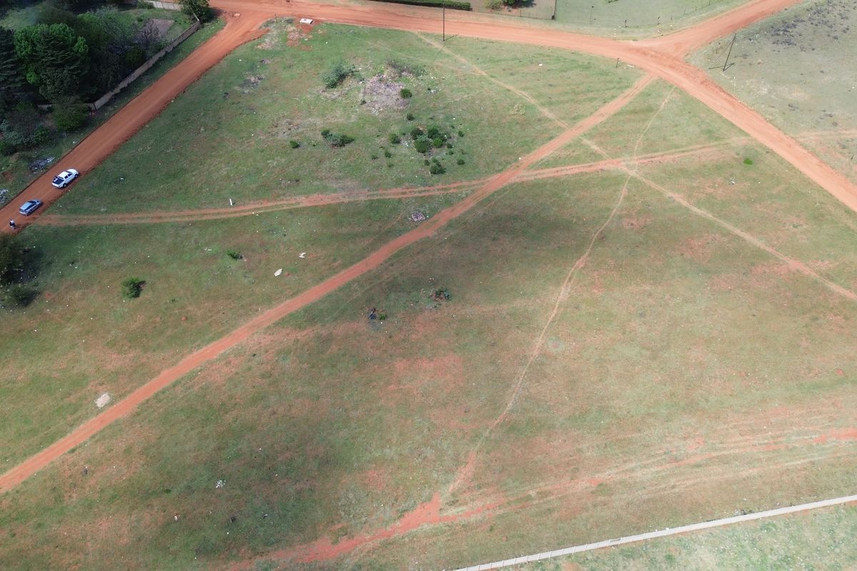 An aerial view of a vacant residential plot featuring natural grass cover and intersecting dirt access roads.