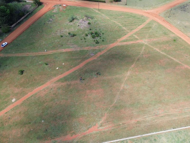 An aerial view of a vacant residential plot featuring natural grass cover and intersecting dirt access roads.