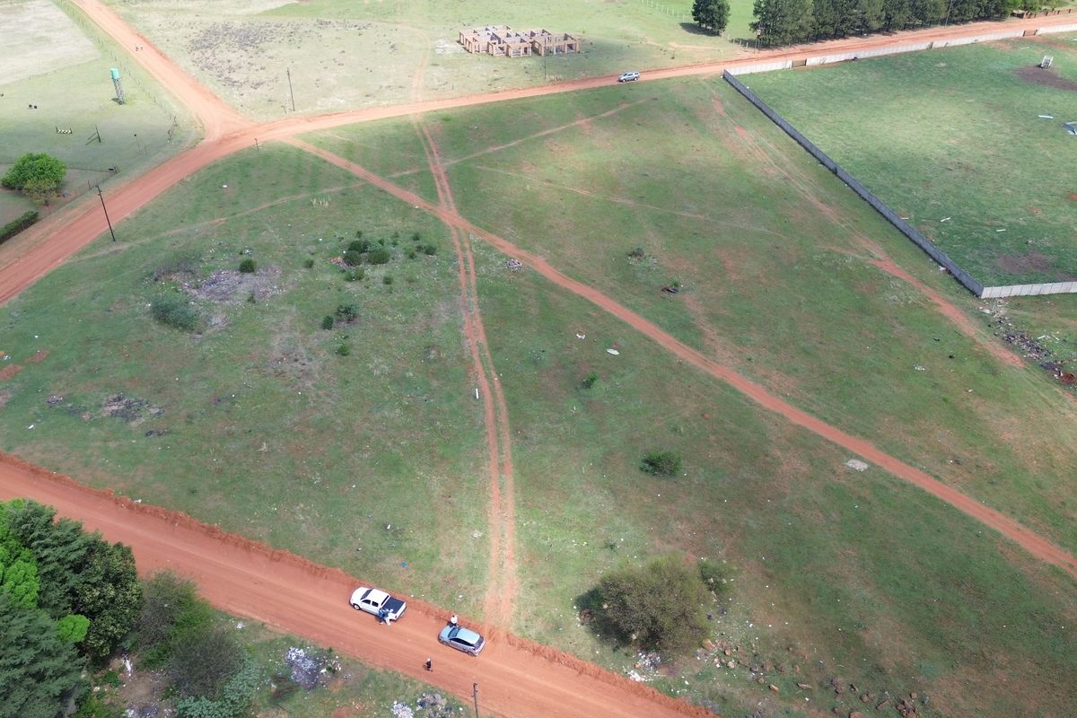 Aerial view of a vacant residential plot featuring dirt road access and surrounding perimeter fencing in a developing area.