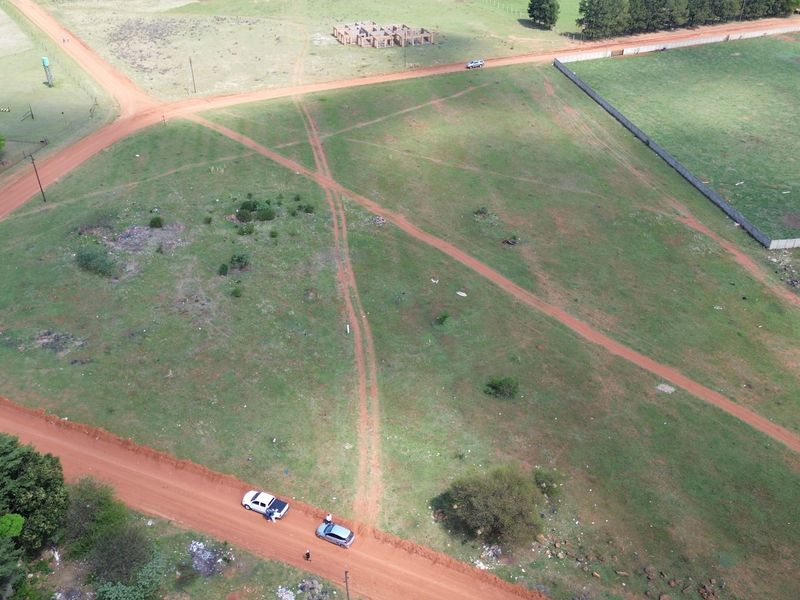 Aerial view of a vacant residential plot featuring dirt road access and surrounding perimeter fencing in a developing area.