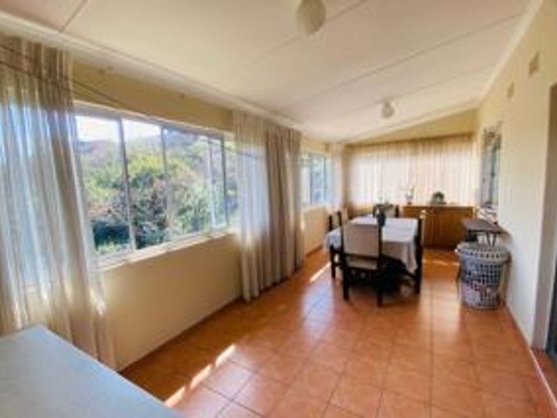 A sunlit enclosed patio or sunroom featuring tiled flooring and large windows with views, offering a versatile space for dining or relaxation.
