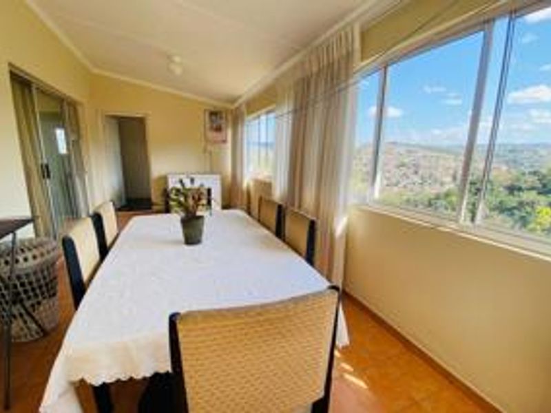 A sunlit dining area featuring large windows with scenic views, tiled flooring, and direct access to the rest of the home.