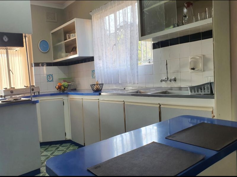 A functional kitchen featuring built-in cabinetry, laminate countertops, a double basin sink, and a tiled backsplash, offering potential for modern updates.