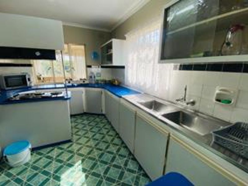 A dated kitchen featuring built-in cabinetry, a double basin stainless steel sink, gas hob, extractor fan, and patterned tiled flooring.